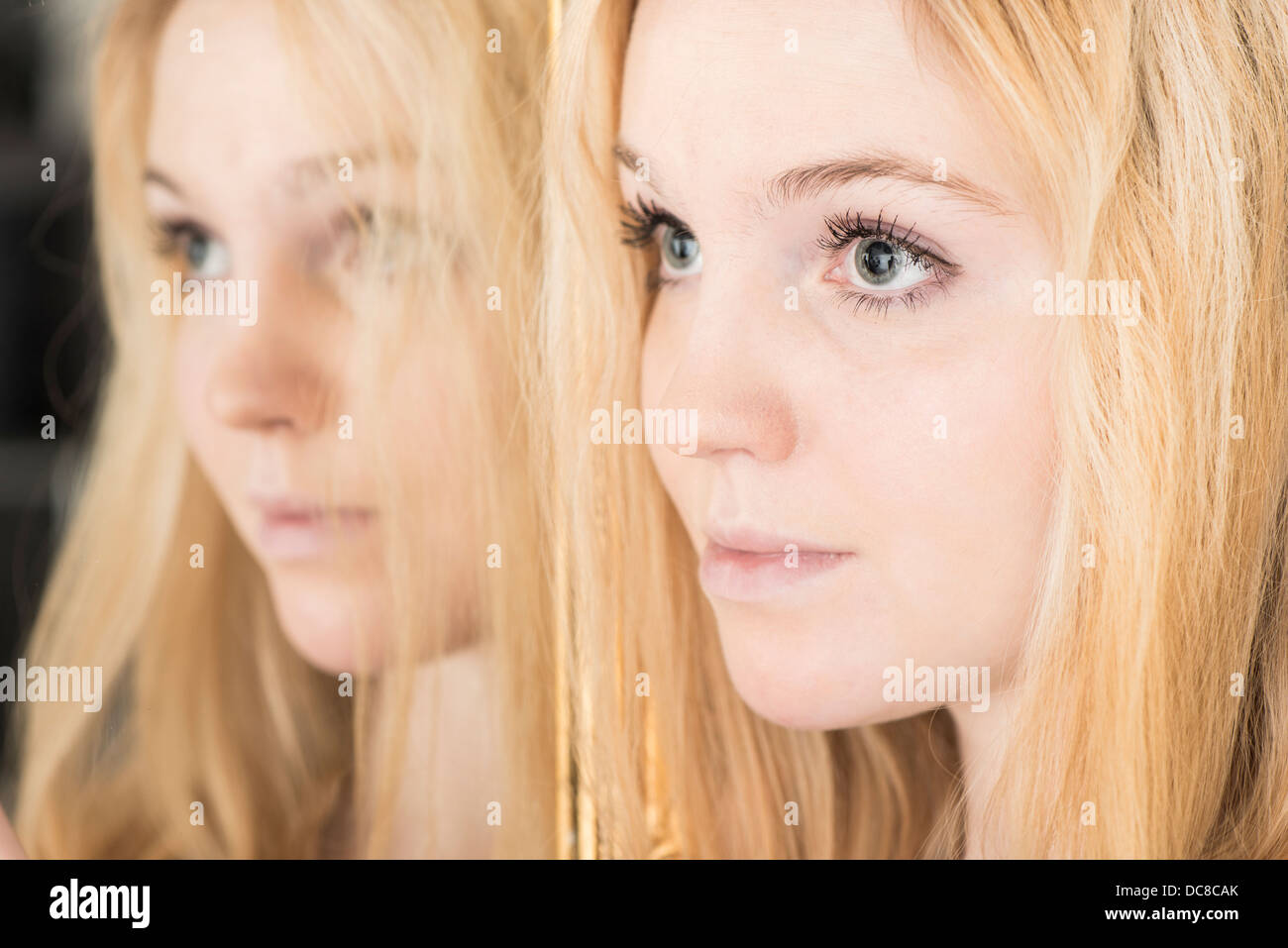 Ritratto di giovane donna bionda adolescente in piedi dallo specchio cercando triste Foto Stock