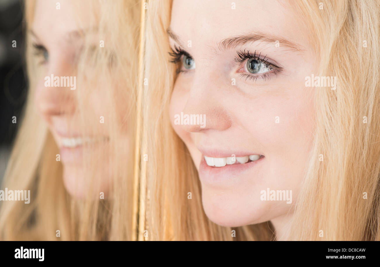 Ritratto di felice bionda e giovane adolescente di sesso femminile in piedi da uno specchio che guarda lontano Foto Stock