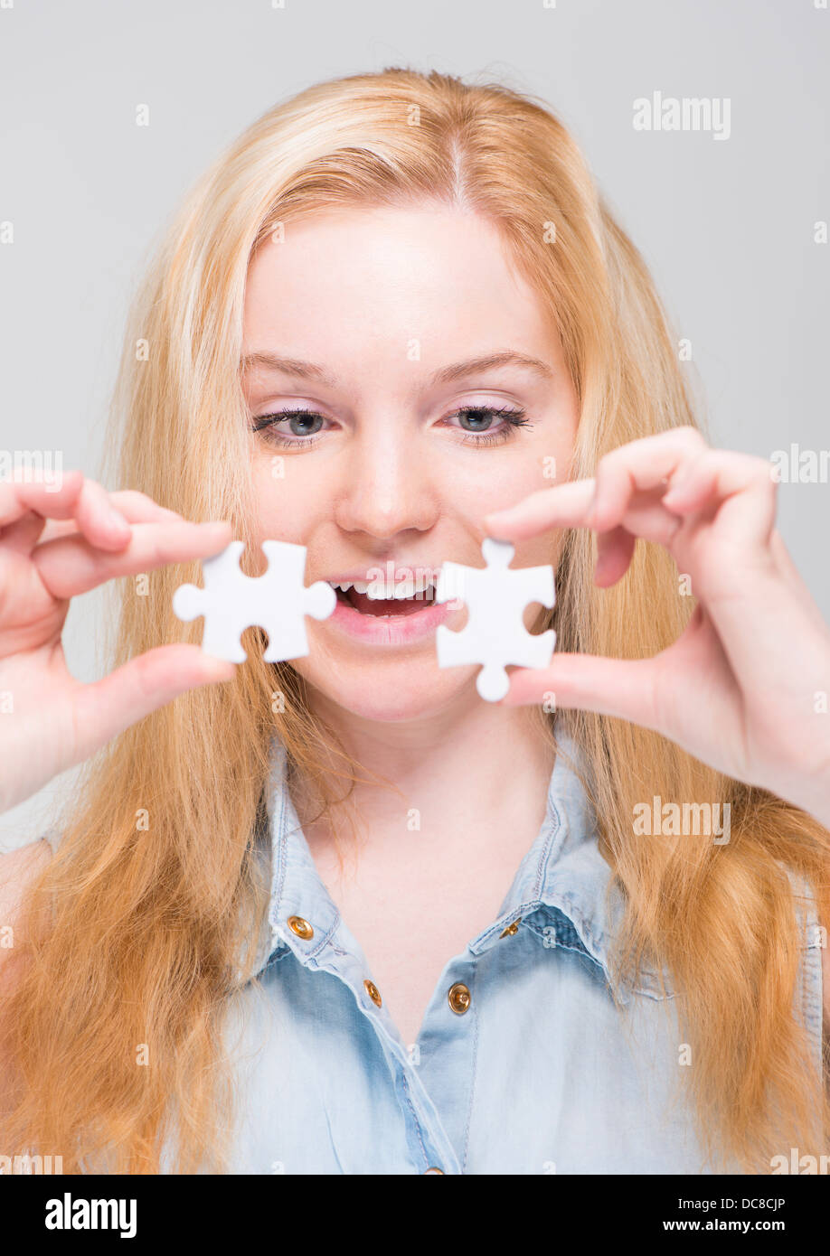 Sorridente giovane donna bionda holding ed esaminando due bianchi i pezzi del puzzle Foto Stock