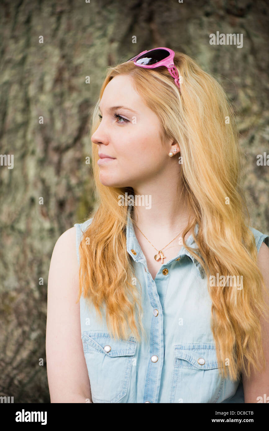 Una bionda e giovane donna attraente di fronte di alberi in un parco Foto Stock