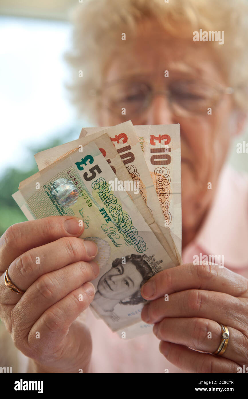 Titolare di pensione o di rendita femmina a casa contando Sterlina Inglese cinque e dieci pound note. Foto Stock