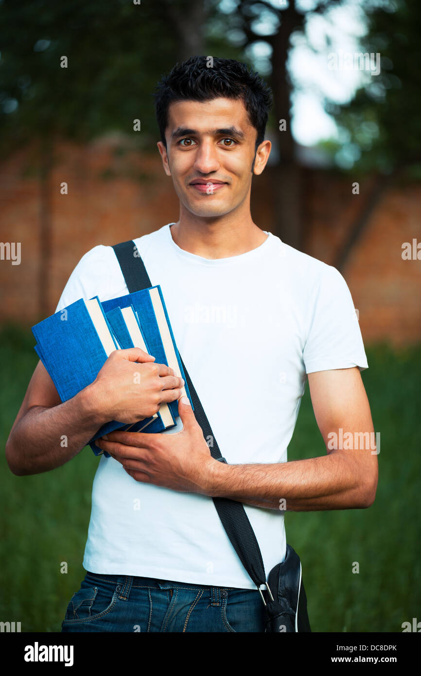 Arabo studente maschio con libri all'esterno guardando molto felice Foto Stock