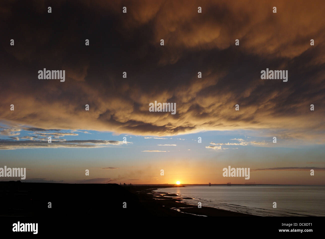 Dark nuvole riflettono il sole di setting su Teesside in Cleveland, Regno Unito Foto Stock