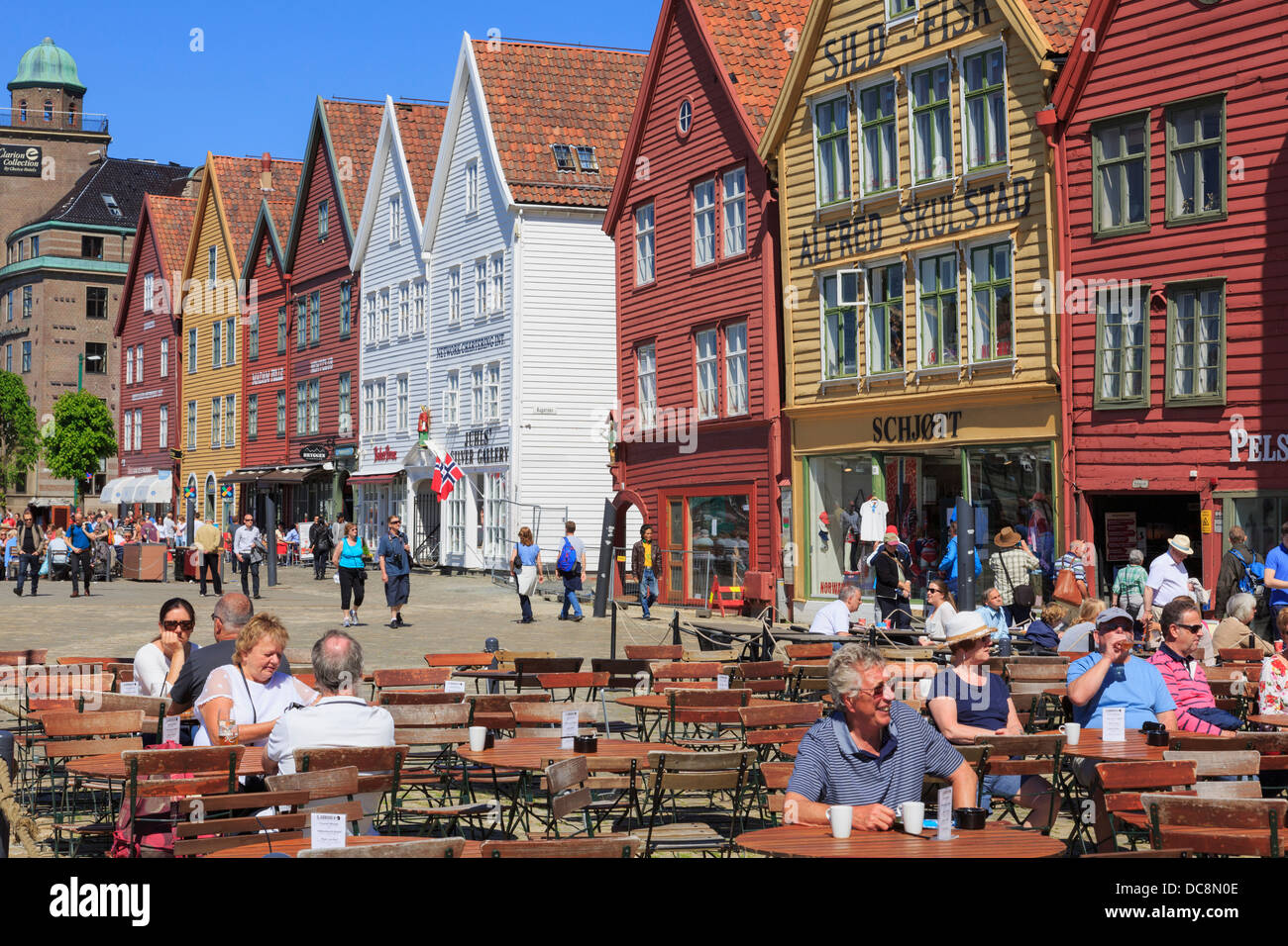 Persone per mangiare fuori in outdoor cafe' sul marciapiede sul lungomare di Bergen storica di edifici in legno in estate. Bryggen a Bergen in Norvegia Scandinavia Foto Stock