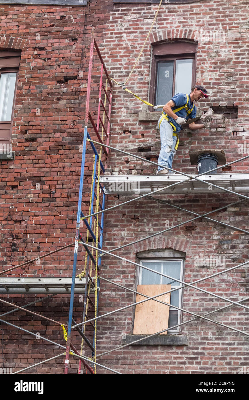 Un mattone muratore funziona su un ponteggio a tre piani per la riparazione di un muro di mattoni in San Giovanni, Nova Scotia, Canada. Foto Stock