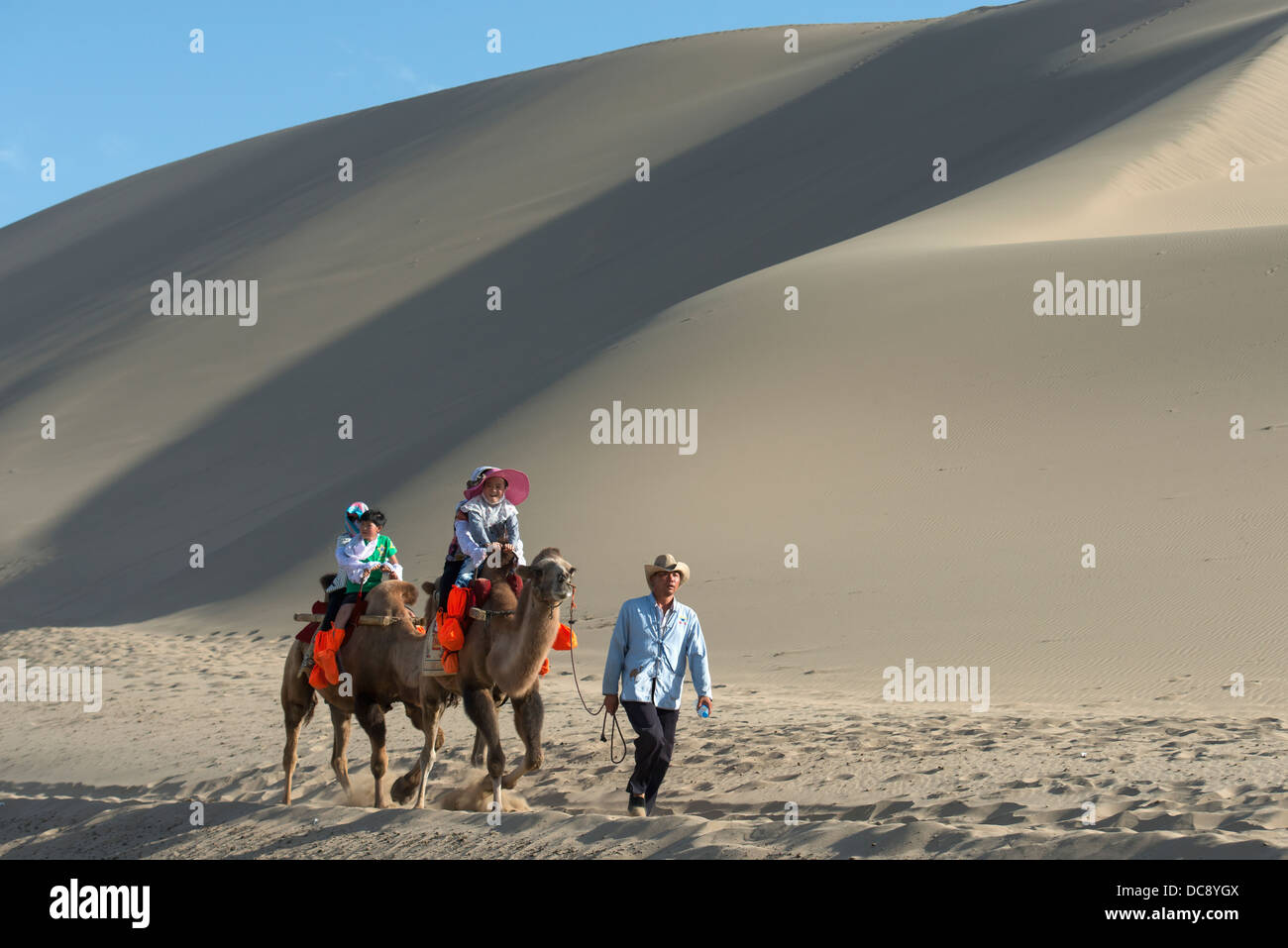 I turisti a cavallo di cammelli a cantare la montagna di sabbia; Jiuquan, Gansu, Cina Foto Stock