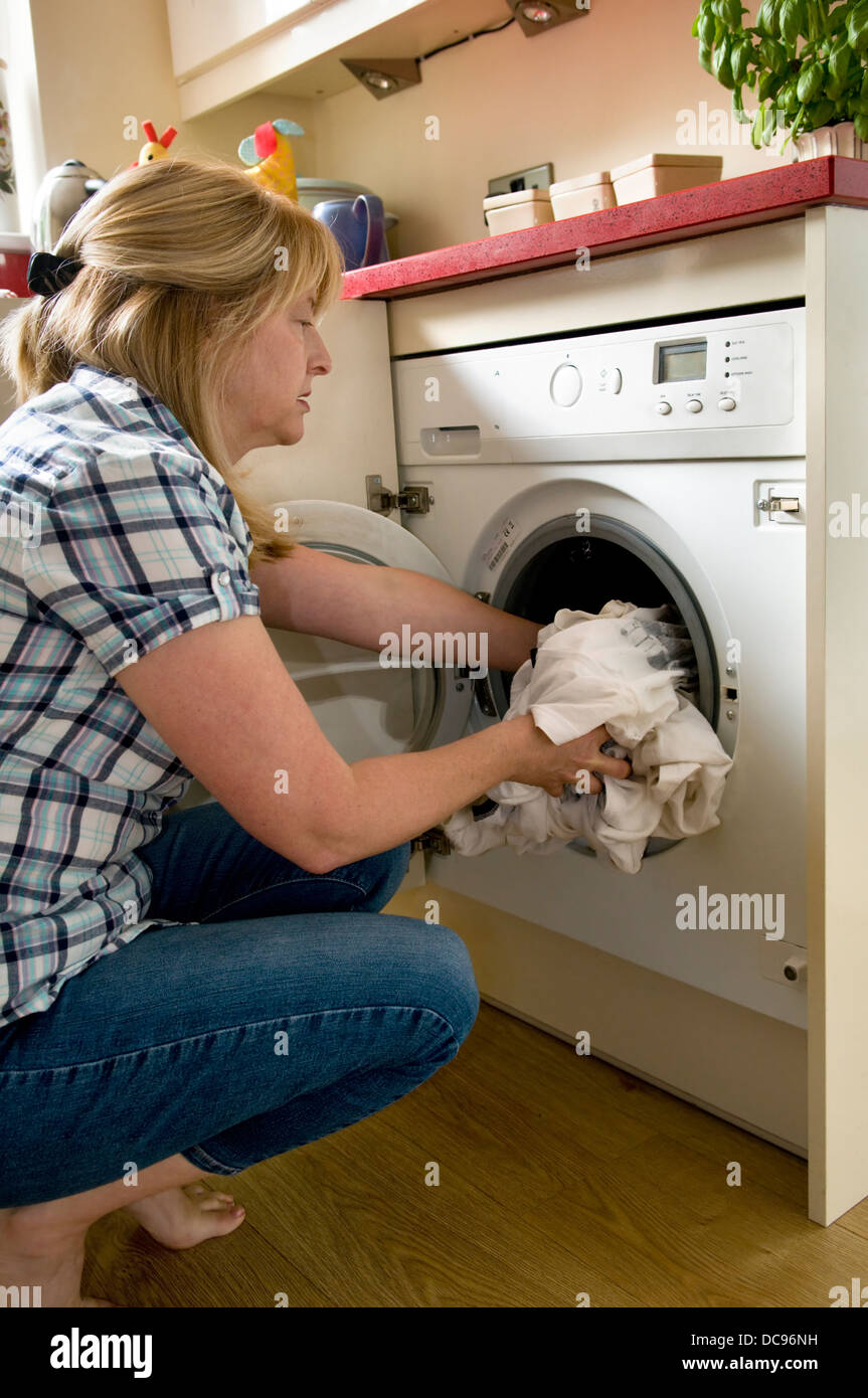 La donna caucasica di caricamento della macchina di lavaggio a casa, prese a Bristol, Inghilterra, Regno Unito Foto Stock