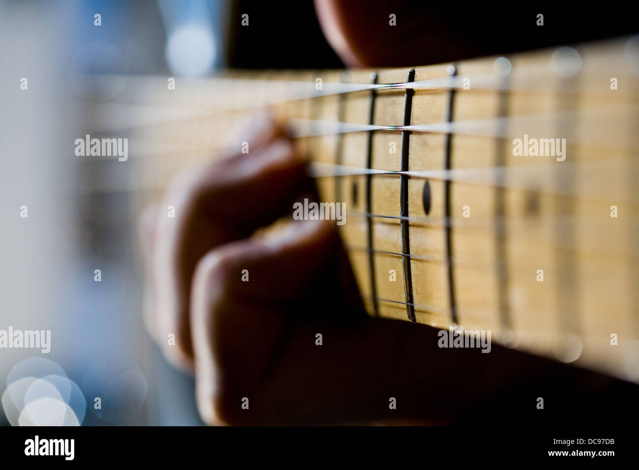 Close-up della tastiera di una chitarra elettrica con una mano fuori fuoco in background Foto Stock