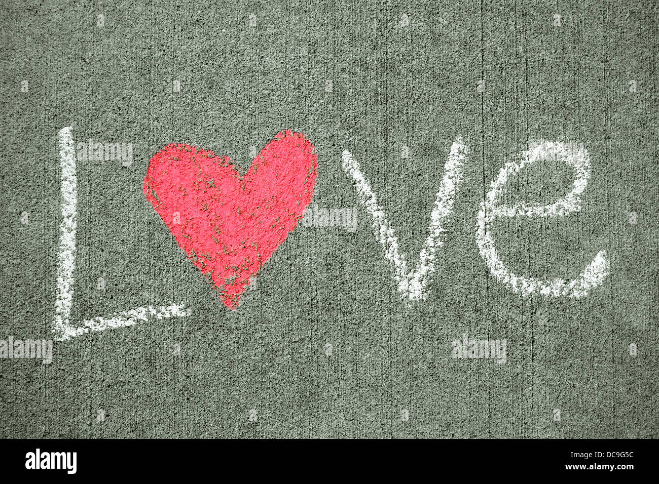 La parola amore è scritta in bianco gesso su un marciapiede e ha un cuore rosa per la lettera o. Foto Stock