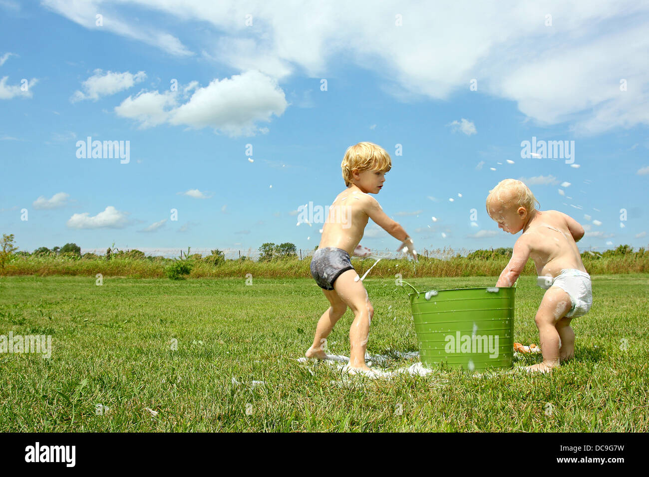 Un bambino e il suo fratellino sono la riproduzione al di fuori su di un giorno di estate con un secchio di acqua saponata, gettando bolle. Foto Stock
