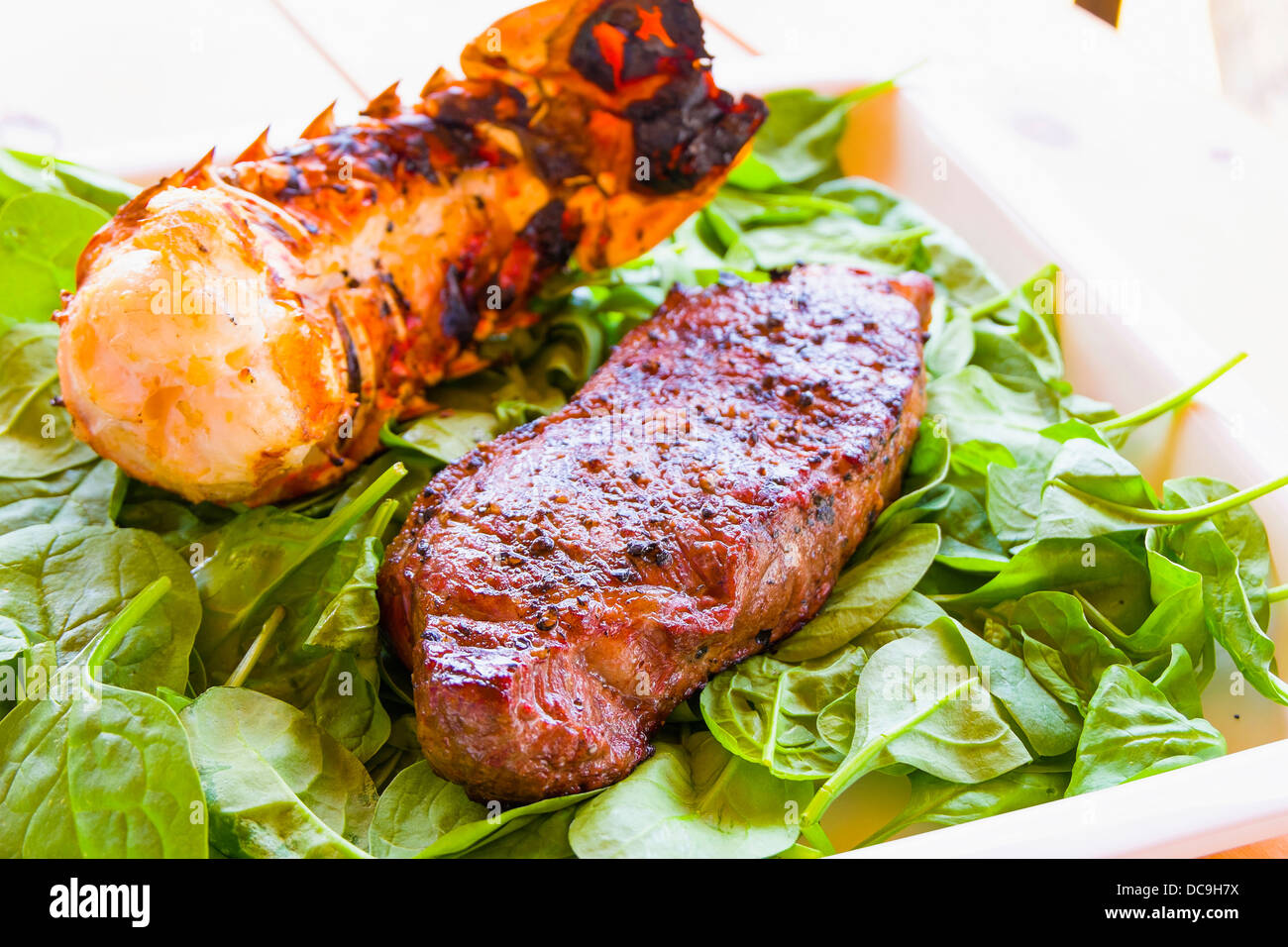 Surf'n Turf Barbecue piatto contenente piatti a base di frutti di mare e bistecche qui Coda di aragosta e New York Strip bistecca su spinaci verde Foto Stock