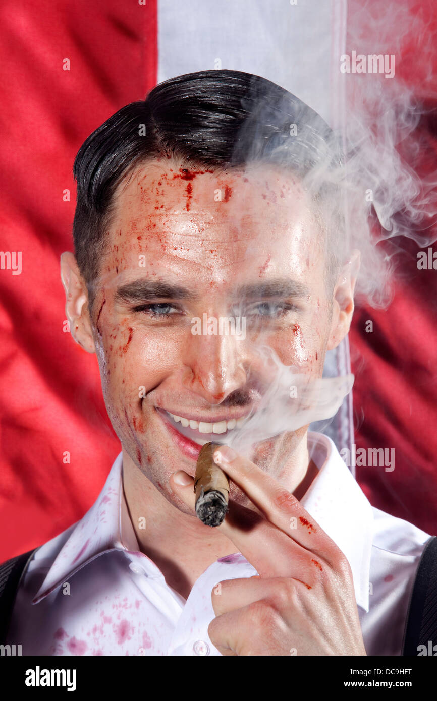 Un uomo con un volto insanguinato di fumare un sigaro di fronte all'American Stars & Stripes bandiera, poste dal modello. Foto Stock