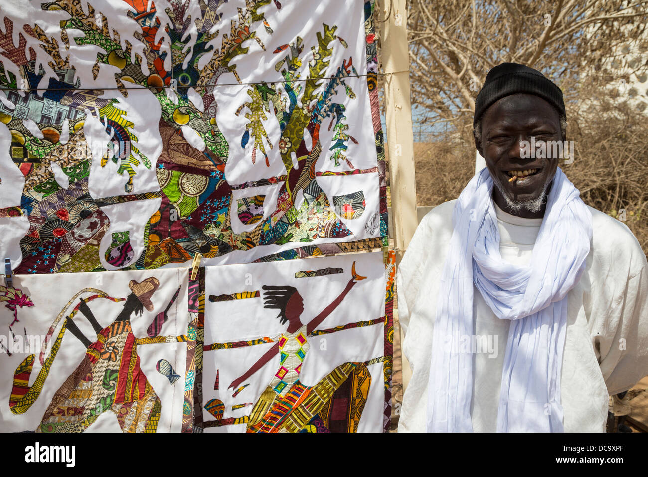 Tessuto artista Bara caduta e le sue creazioni, isola di Goree, Senegal. Egli ha un chewing stick nella sua bocca, per la pulizia dei denti. Foto Stock