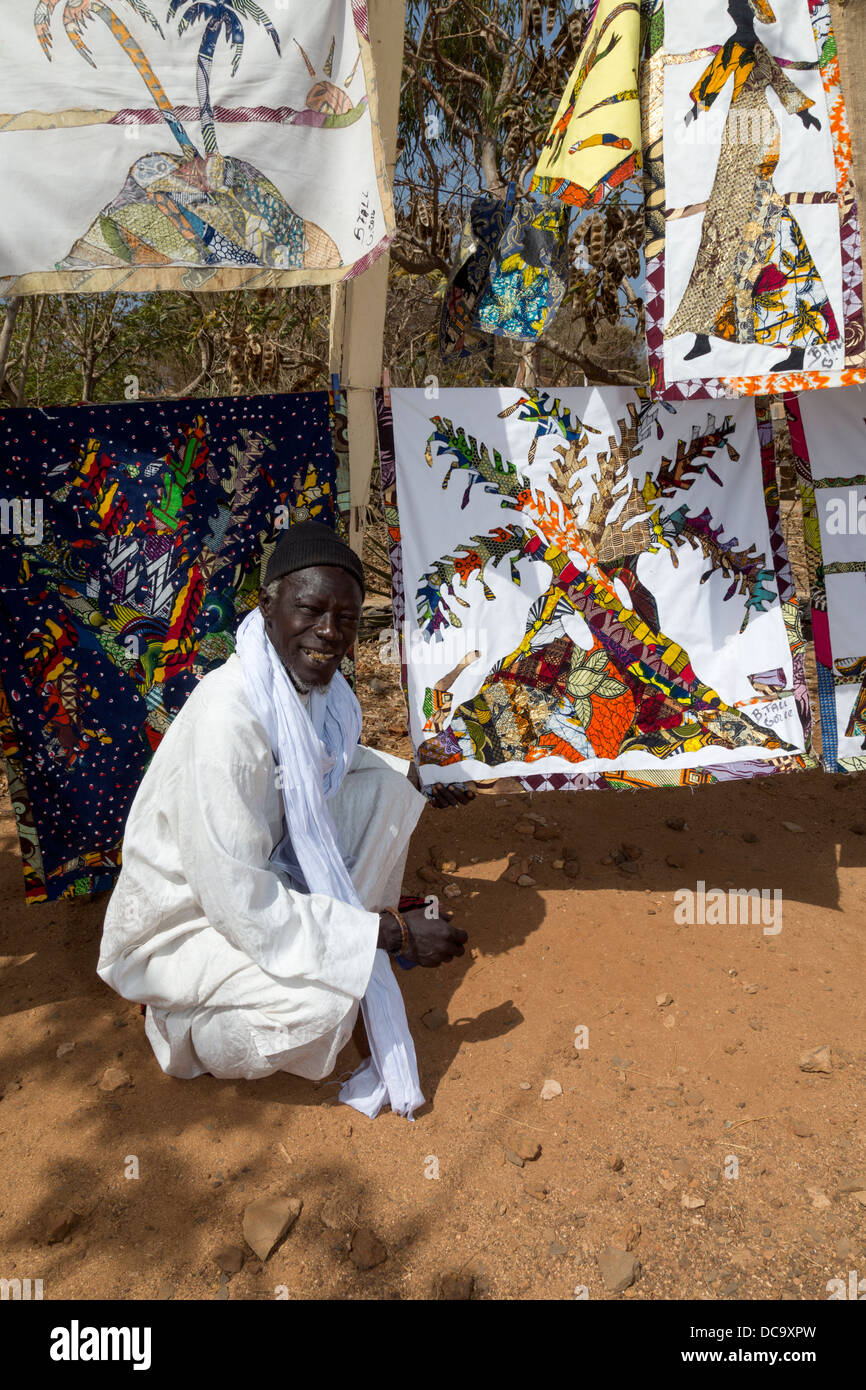 Tessuto artista Bara caduta e le sue creazioni, isola di Goree, Senegal. Egli ha un chewing stick nella sua bocca, per pulire i denti. Foto Stock