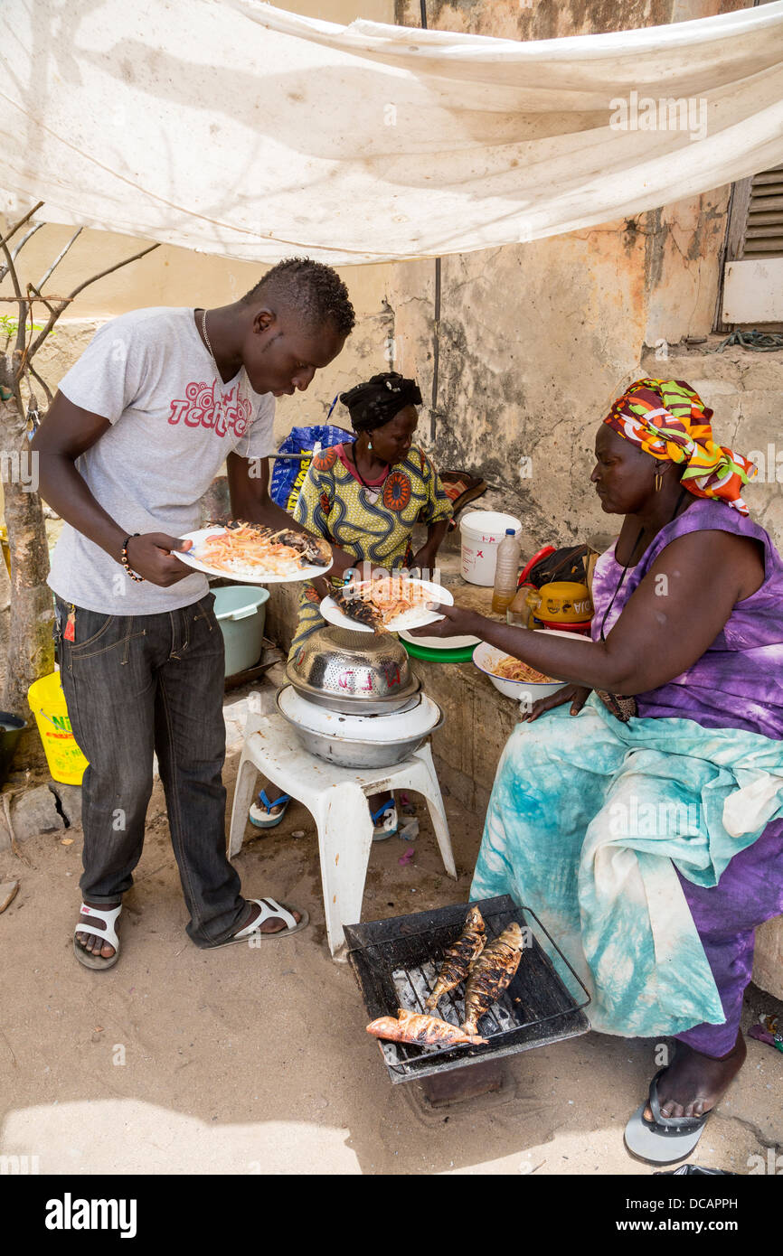 I clienti che acquistano il pranzo di grigliate di pesce, riso e cipolle di street-food Vendor, isola di Goree, Senegal. Foto Stock