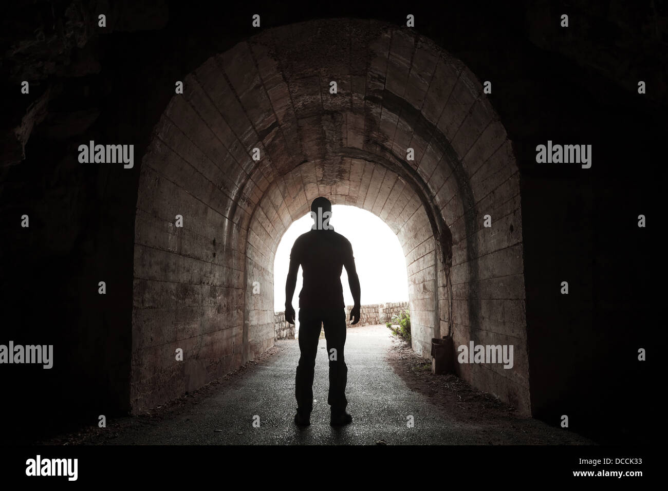 Giovane uomo sorge nel buio del tunnel e si affaccia nel finale incandescente Foto Stock