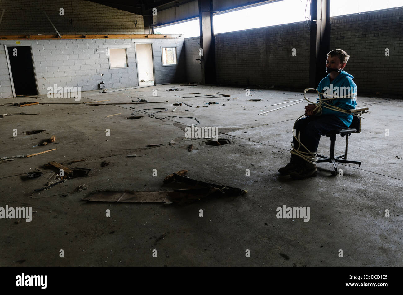 Un ragazzo è tenuto in ostaggio e legato ad una sedia in un magazzino vuoto Foto Stock
