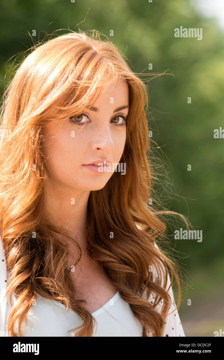 Ragazza con lunghi capelli rossi guardando la fotocamera con alberi in background Foto Stock