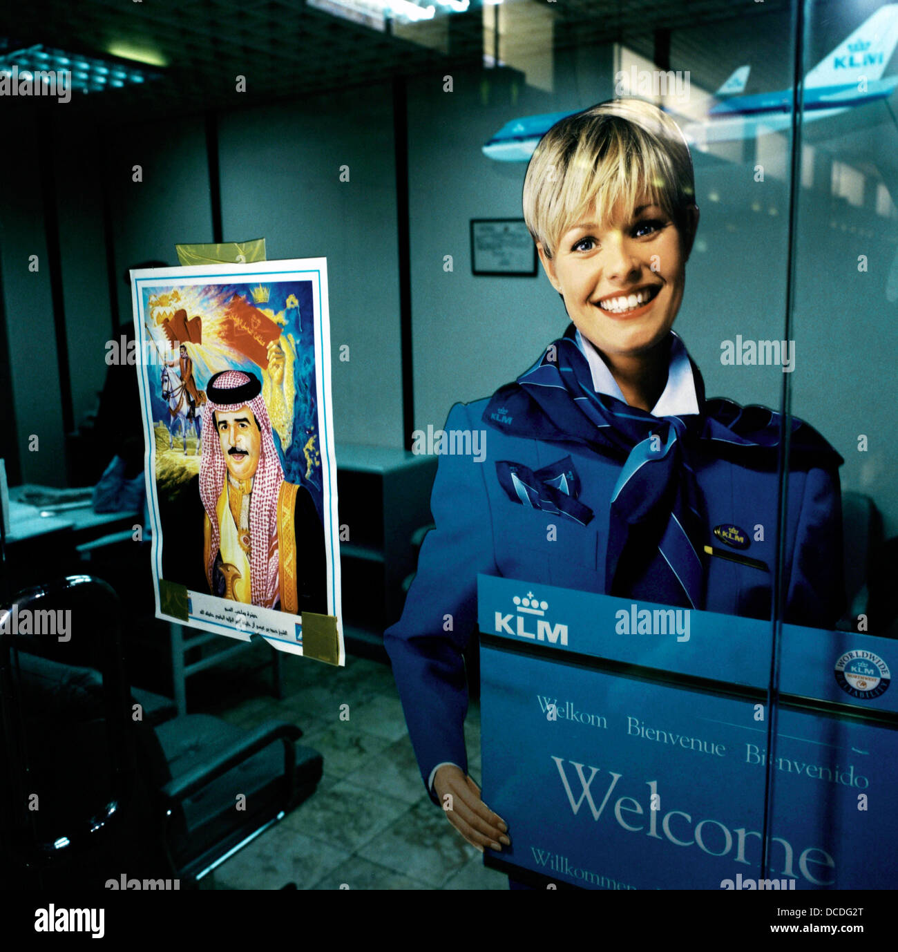 Ufficiale accanto al ritratto di una reale Bahraini stati, il volto sorridente di una bionda olandese della compagnia aerea KLM ragazza adorna di un poster in compagnia dell'ufficio in aeroporto Bahrain Foto Stock
