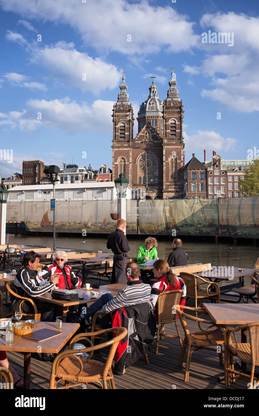 I turisti a pranzo in ristorante cafe dal canale ad Amsterdam, nei Paesi Bassi, la chiesa di San Nicola in background. Foto Stock