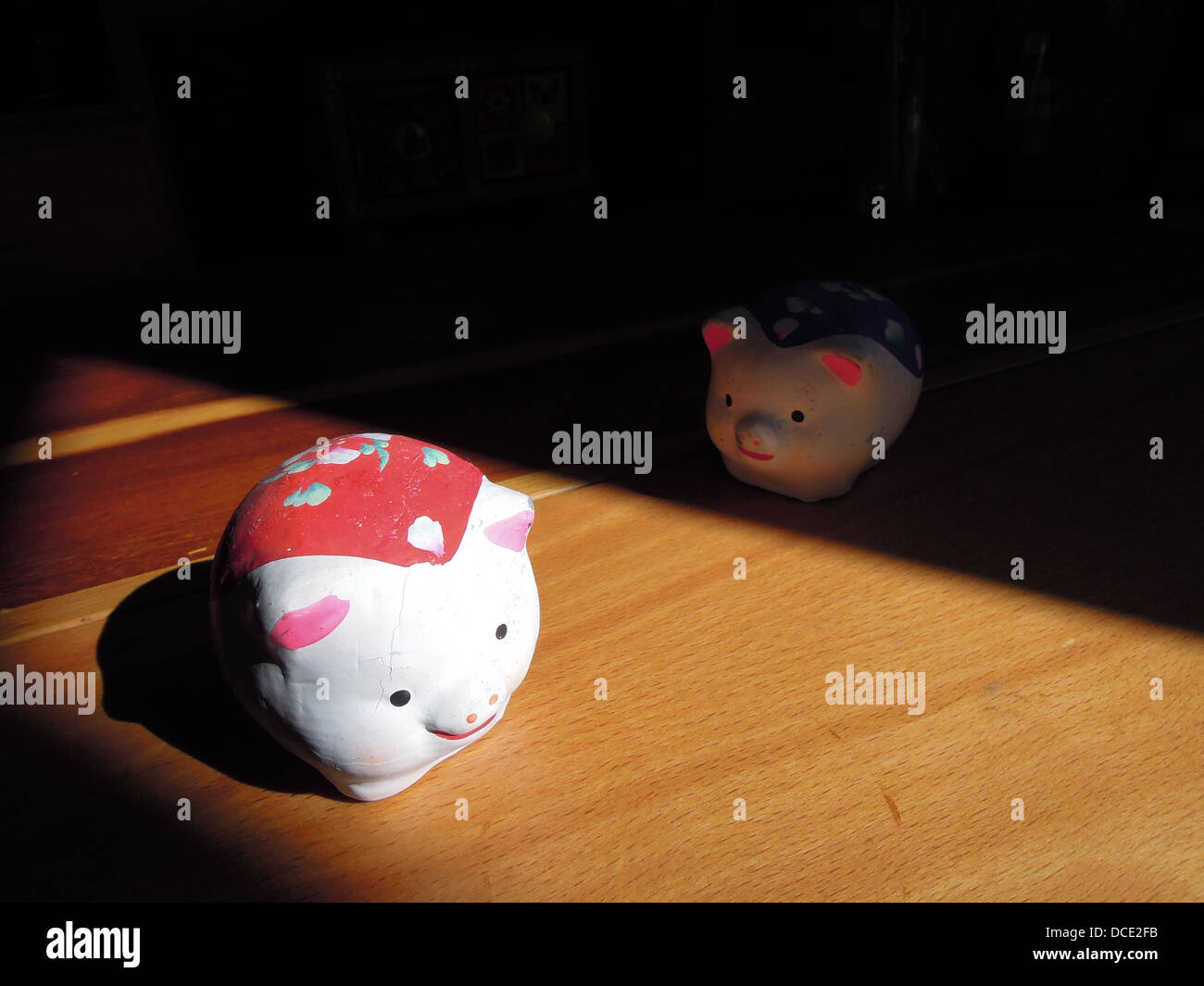 Due piccoli graziosi colorati scultura in argilla suini provenienti dalla Cina quello blu nel buio guardando quella rossa sotto il sole Foto Stock