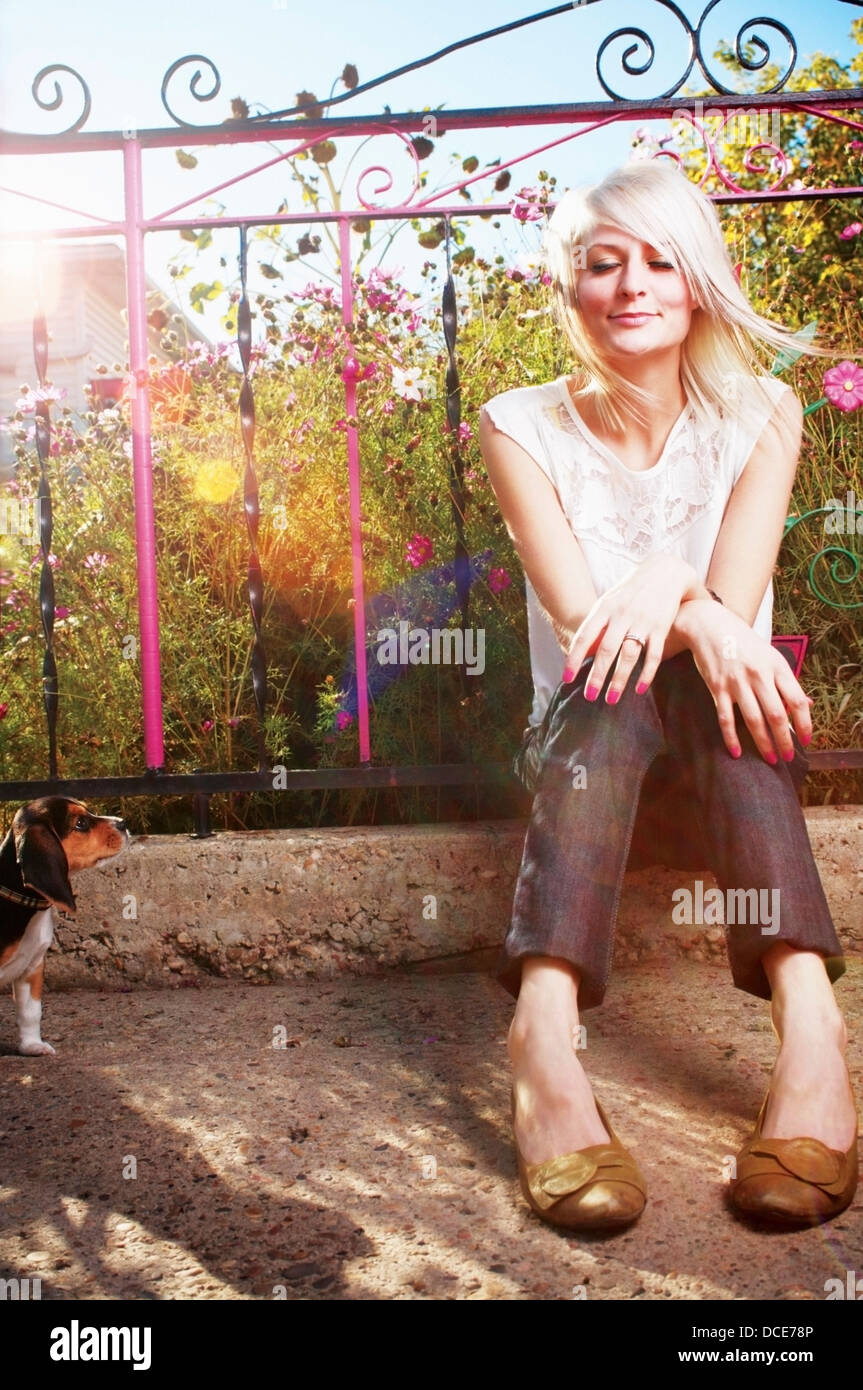 Giovane, Bella donna bionda seduti in giardino mentre gli orologi del cane il suo Foto Stock