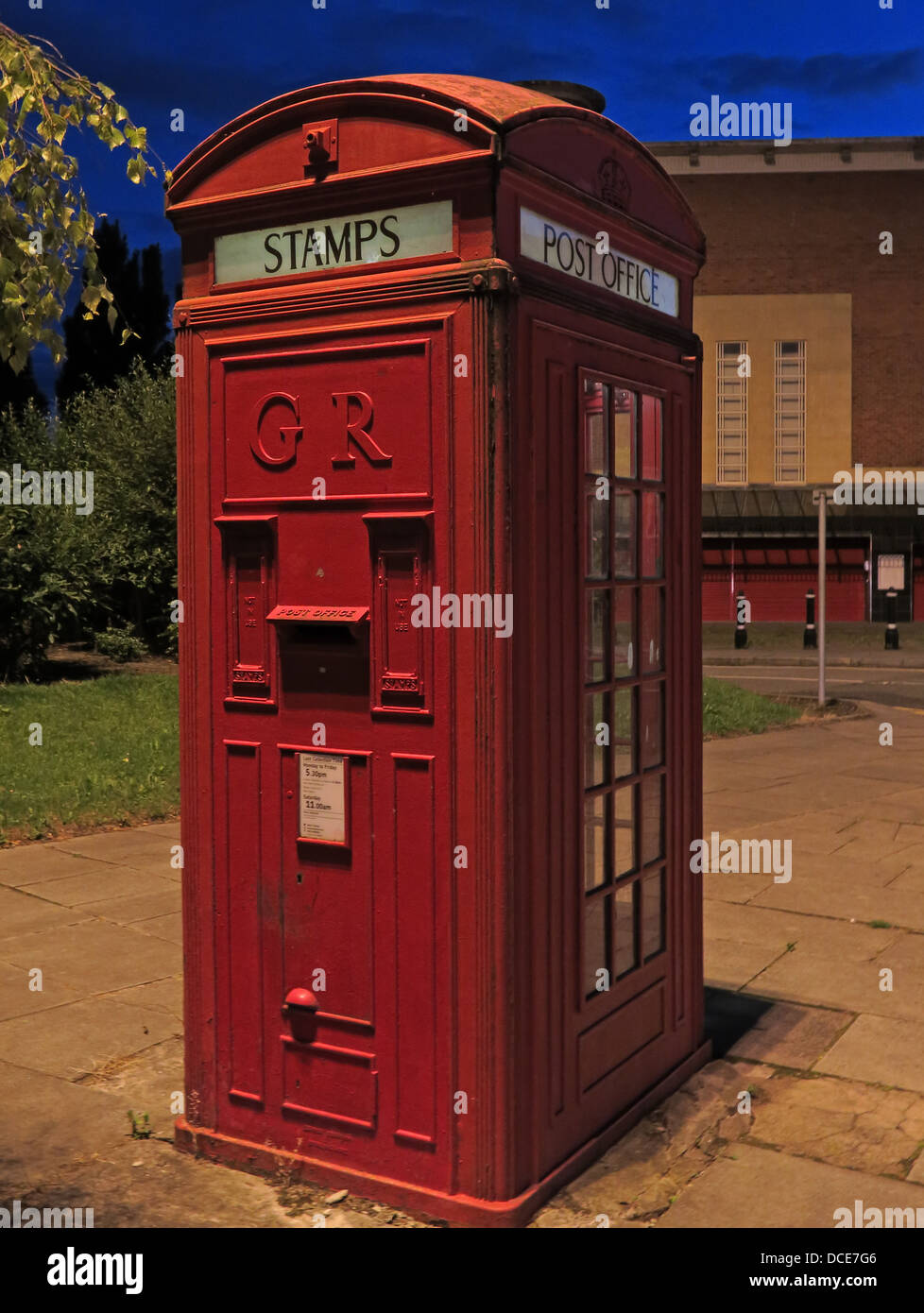 Red K4 nella casella Telefono che vendevano francobolli GR al crepuscolo, Warrington, Cheshire, NW Inghilterra, Regno Unito WA1 Foto Stock