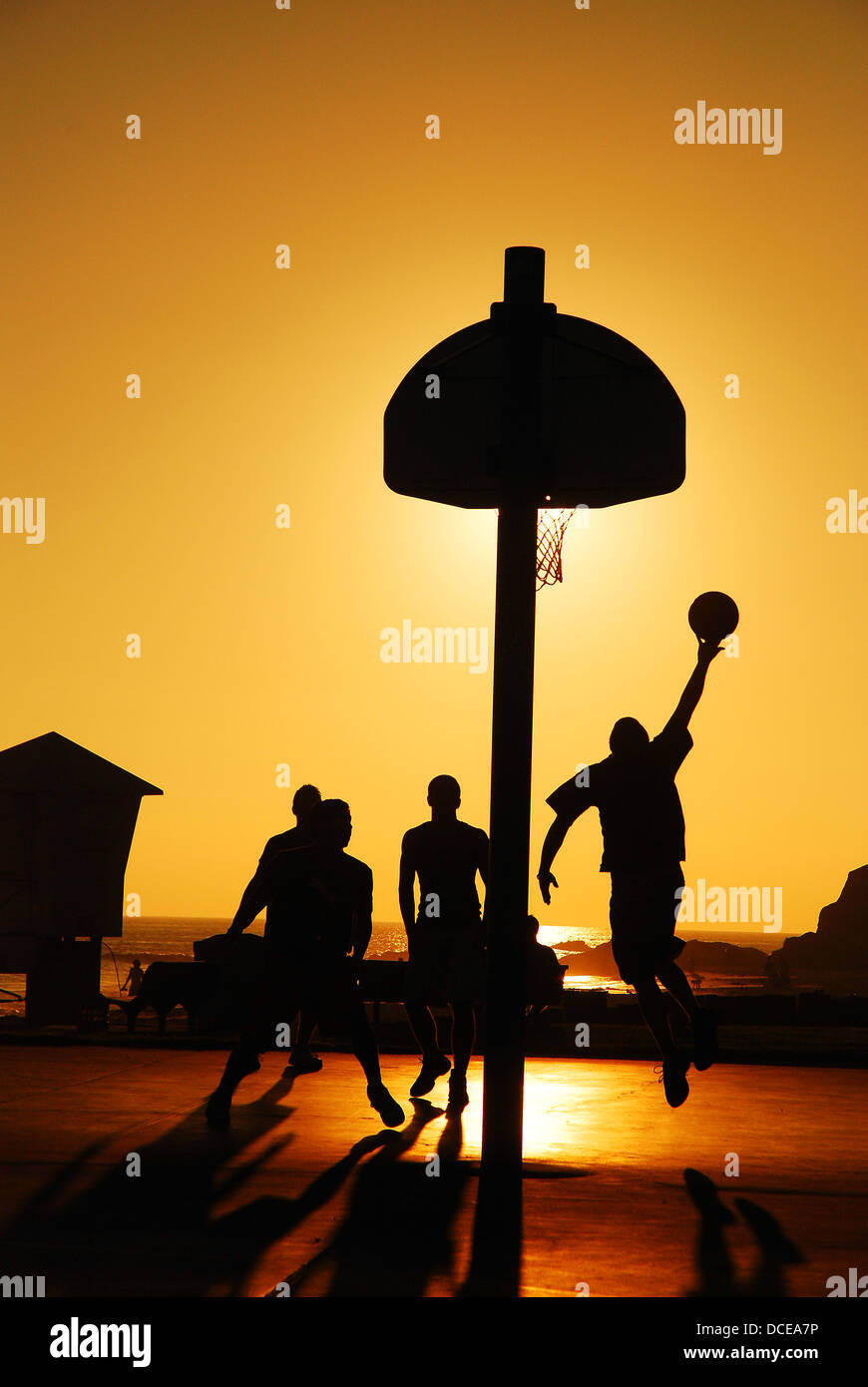 Un gruppo di amici che giocano a un pick up gioco di basket come il sole tramonta Foto Stock