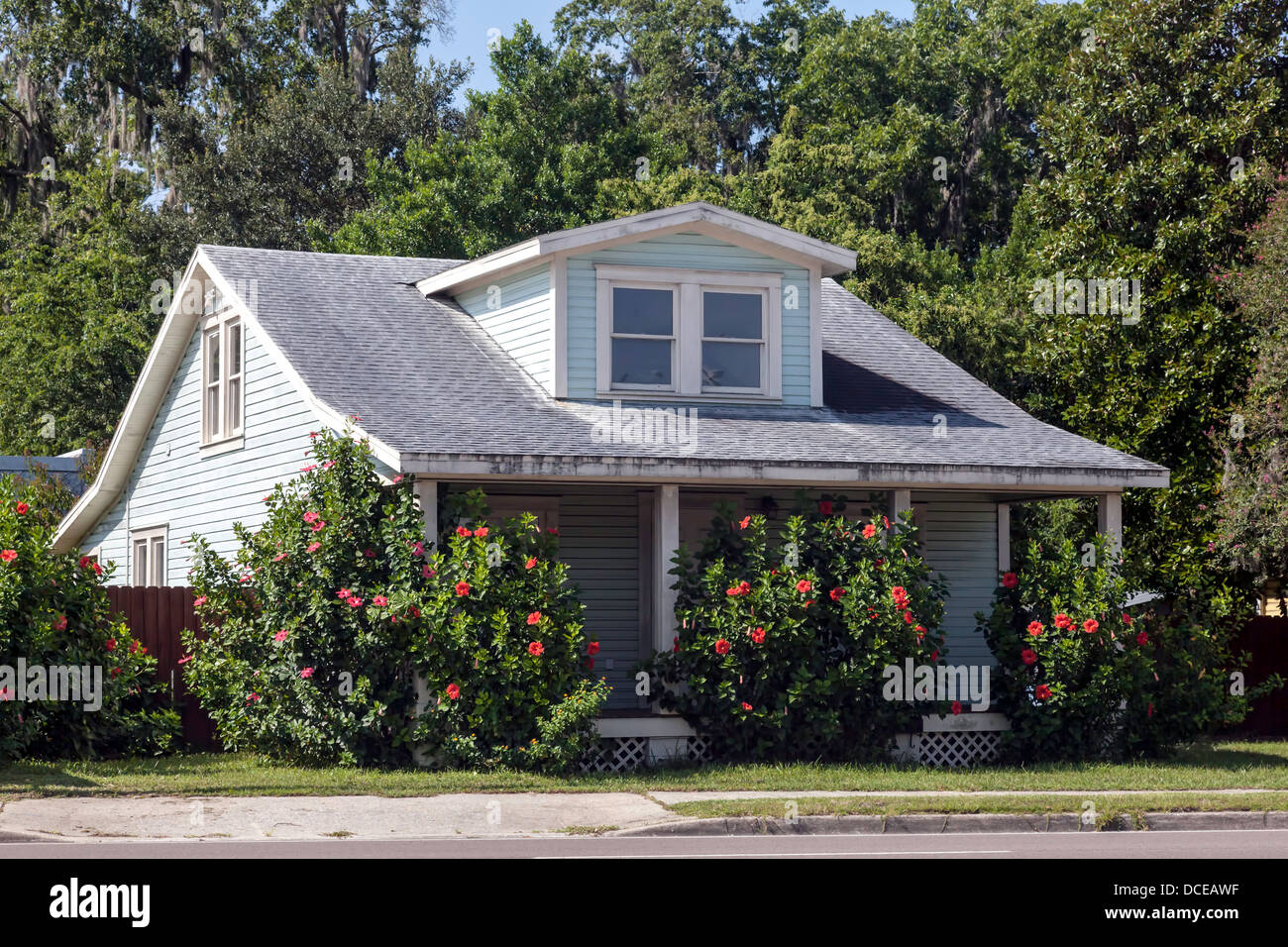 Colore blu pallido, 2-story clapboard bungalow con finestre dormer, rivestimento bianco e portico veranda e hibiscus cespugli. Foto Stock