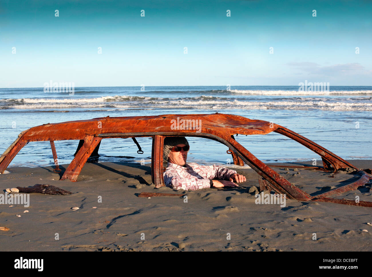 Uomo si siede in auto arrugginito relitto sepolto nella sabbia sulla spiaggia Foto Stock