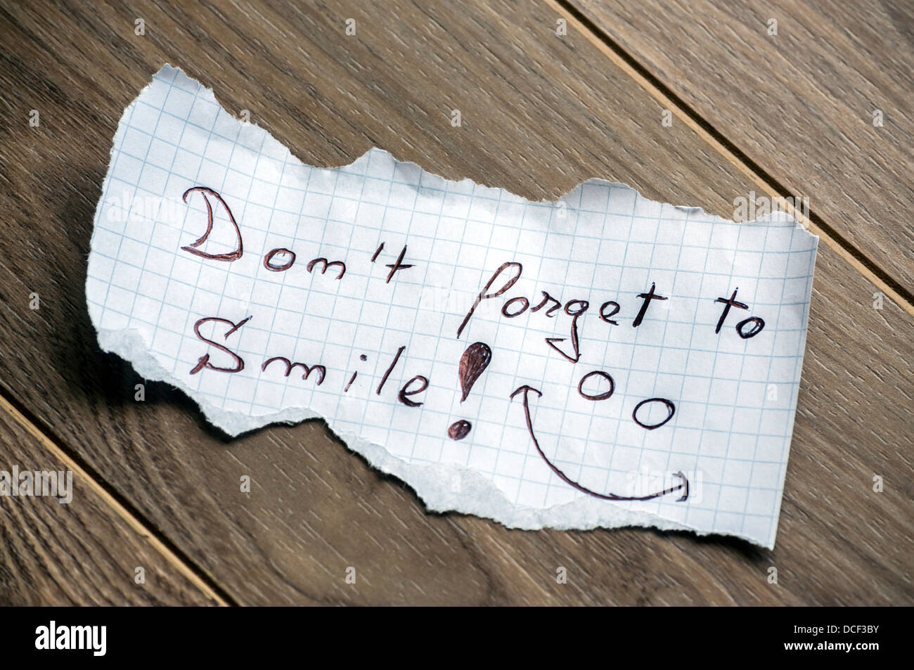 Non dimenticate di sorridere - La scrittura a mano il testo su un pezzo di carta su uno sfondo di legno Foto Stock