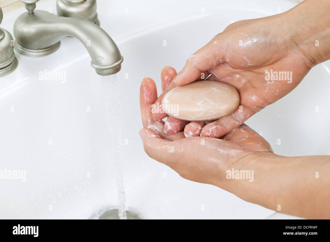 Foto orizzontale di mani femminili di formazione di schiuma con barra di sapone, acqua e il lavandino del bagno in background Foto Stock
