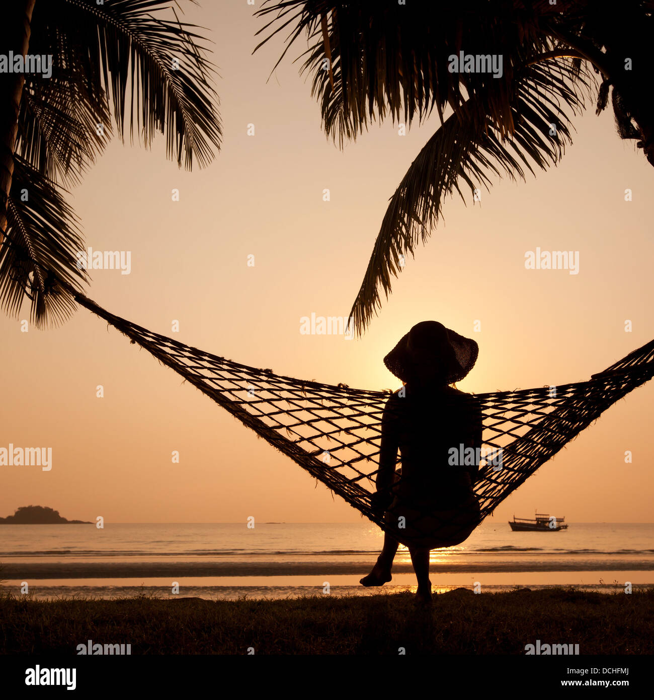 Donna in amaca godersi il tramonto sulla spiaggia Foto Stock