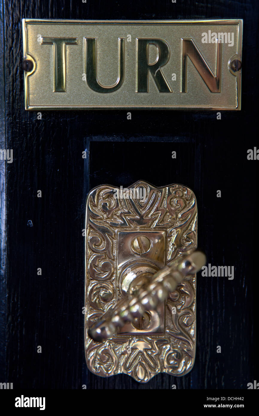 Una vista dettagliata di una tornitura di ottone campanello su una porta nera con il segno che legge giro. Foto Stock