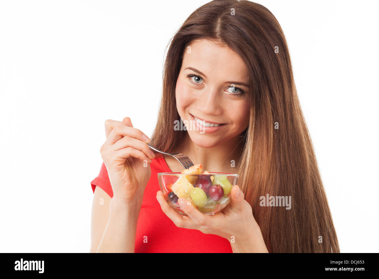 Giovane donna mangiare frutta e sorridente, isolato su bianco Foto Stock