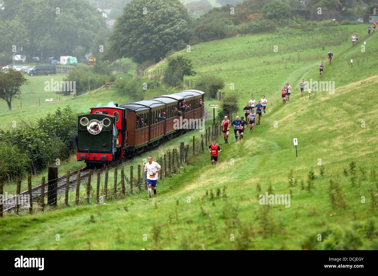 Tywyn, Wales, Regno Unito, Sabato, 17 agosto 2013 nella foto: atleti racing contro un treno a vapore vicino Tywyn, Galles. Re: gara il treno è un annuale cross country in esecuzione evento che avviene in Tywyn, metà del Galles. La gara è organizzata da Tywyn Rotary Club, e attrae corridori provenienti da tutto il mondo. Nel main event, corridori competere per battere un treno a vapore su conserve Talyllyn Railway su una distanza di 14 miglia (23 km). La manifestazione è stata l'idea di dentista locale, Godfrey Worsey, e fu eseguita per la prima volta nel 1984 con circa 48 guide. © D Legakis/Alamy Live News Foto Stock