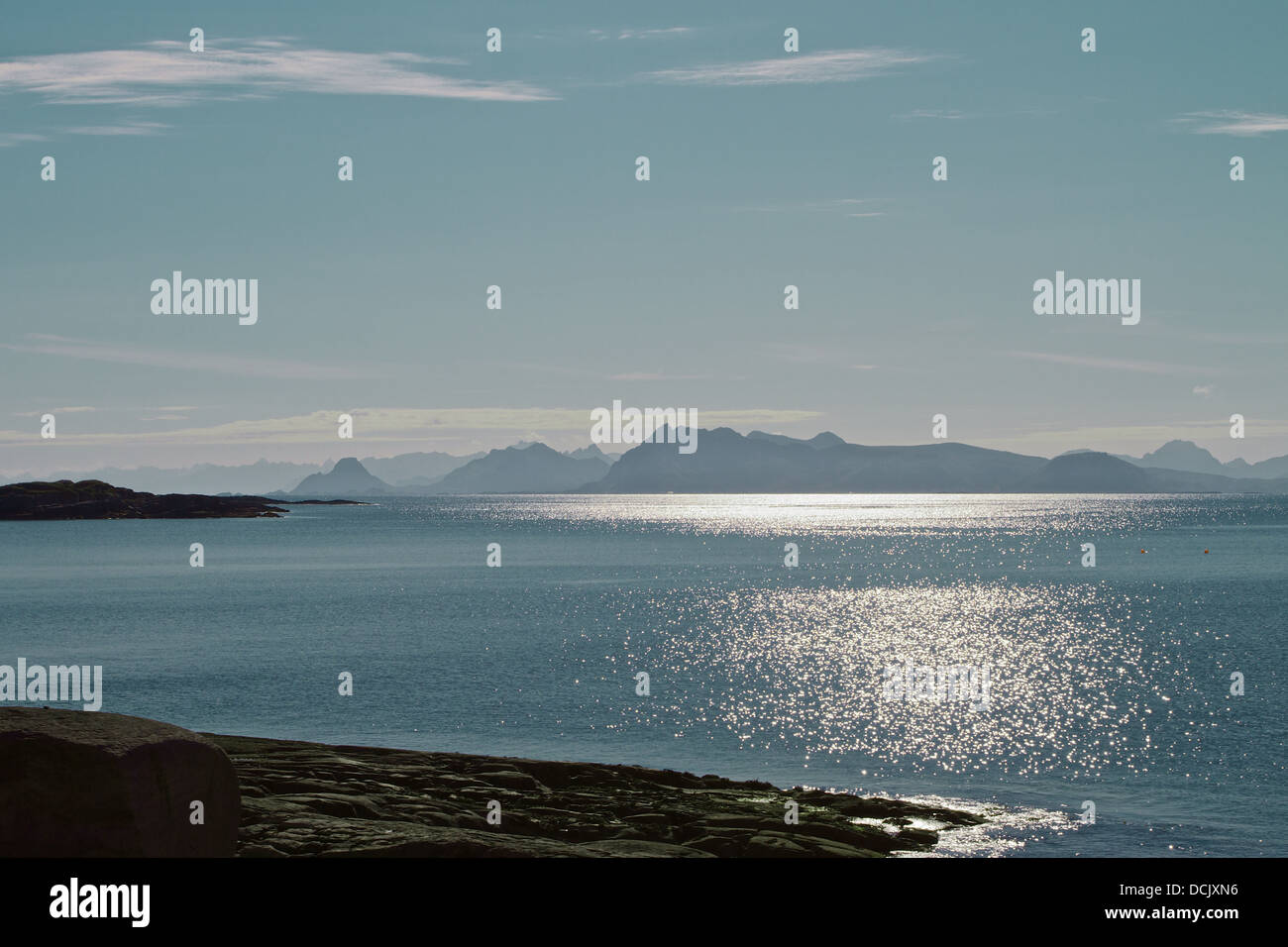 Bassa Arctic Sun in un puro cielo blu riflettendo sull'oceano scintillante con isole montagnose in background Foto Stock