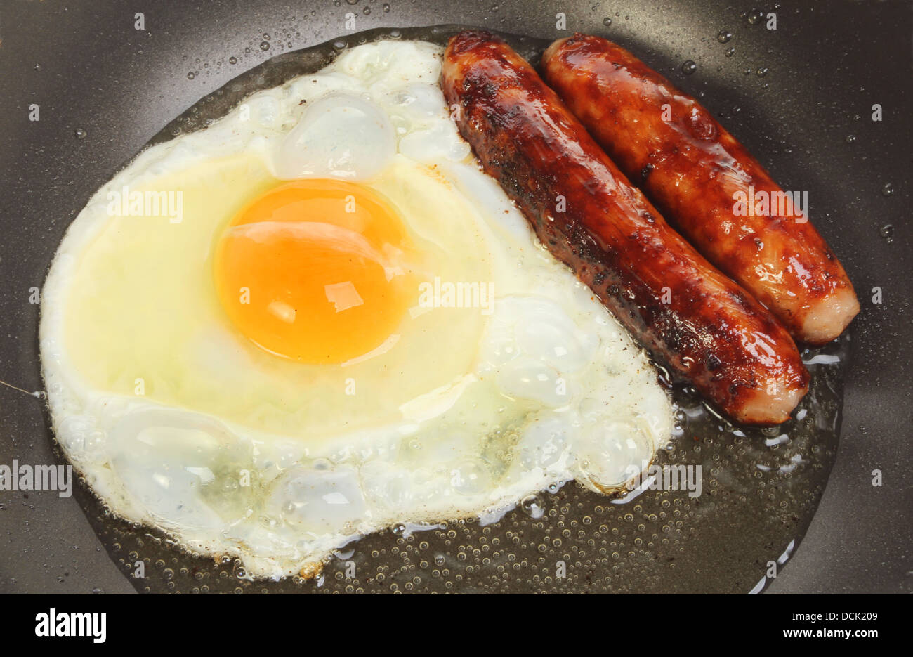 Primo piano di salsicce e di un uovo friggere in una padella Foto Stock
