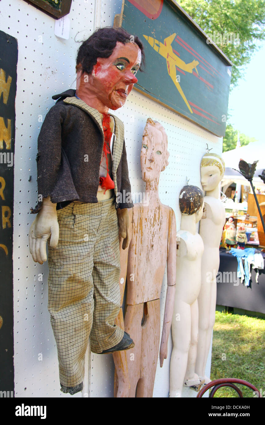 Un dipinto e vestito di legno vintage ventriloquo fantoccio appeso su una parete accanto ad altre bambole in legno e arte in un mercato delle pulci. Foto Stock