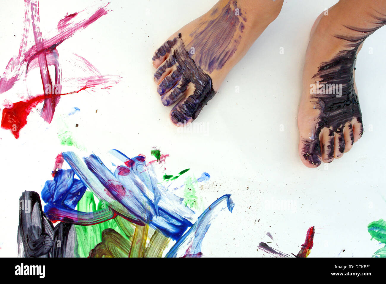 Vicino a un piccolo bambino i piedi che sono coperti di vernice, in piedi su un grande vuoto di carta bianca con dipinti colorati Foto Stock