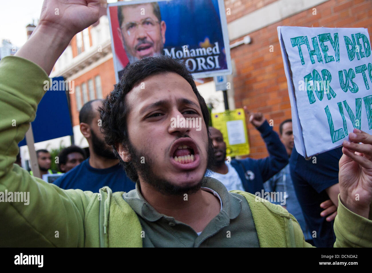 Londra, 20-08-2013. Un uomo chants slogan e visualizza il suo striscione al di fuori dell'ambasciata egiziana come parte delle proteste in corso contro il colpo di stato militare del deposto presidente morsi di governo democraticamente eletto. Foto Stock