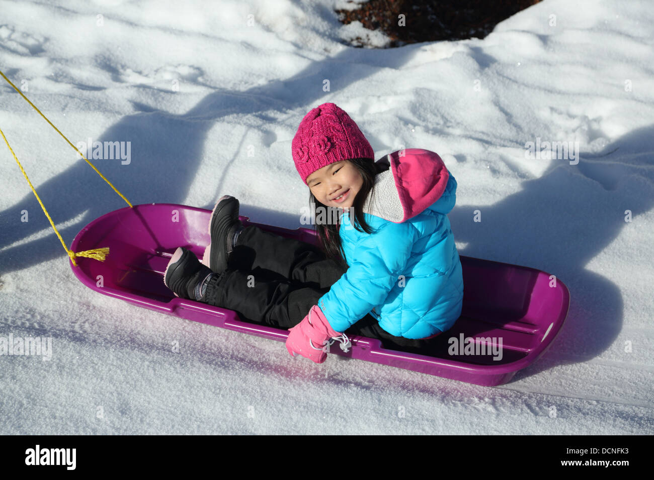 Giovane ragazza asiatica sulla slitta nella neve Foto Stock