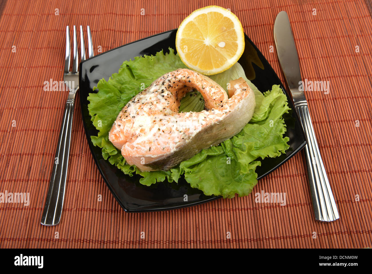 Delizioso salmone cotto su lattuga con il limone a piastra nera Foto Stock