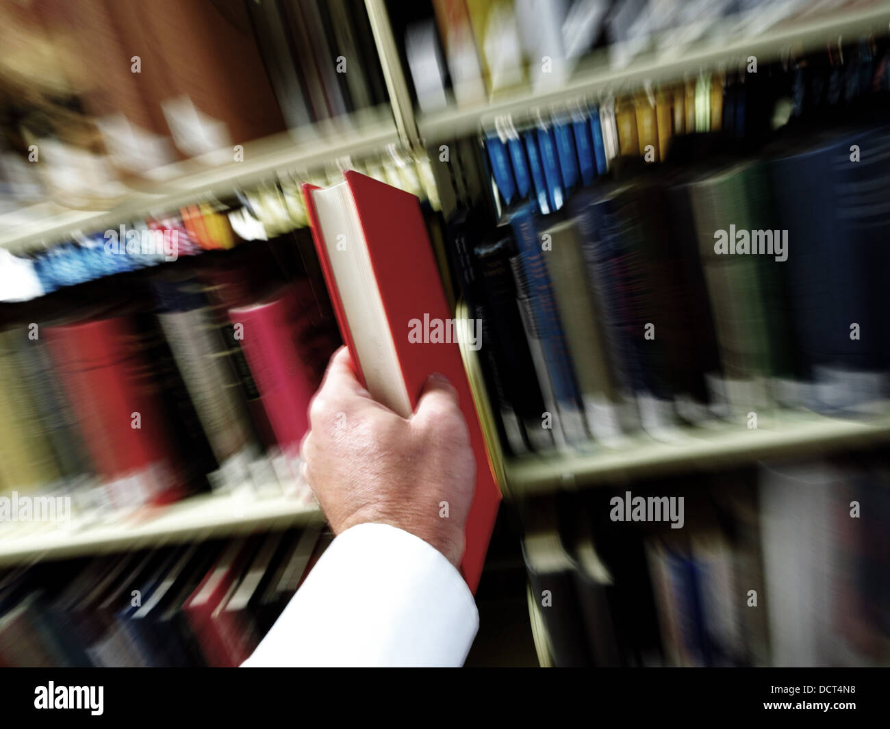 Le mani tirando un libro rosso dal ripiano con Libreria in background Foto Stock