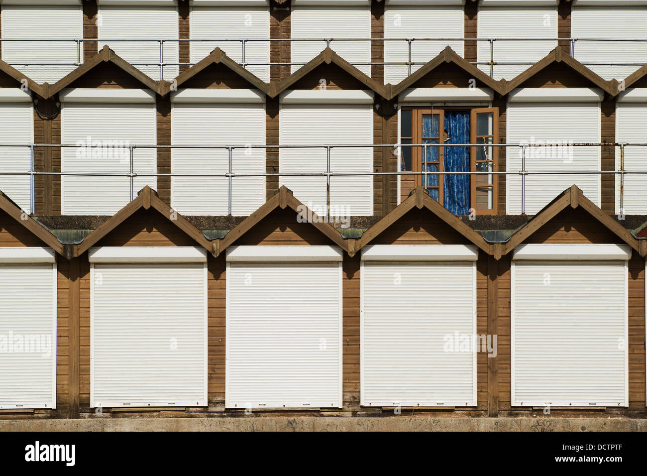 File sovrapposte di spiaggia di capanne con porte bianco a Swanage, Dorset, rendendo modello geometrico rotto da uno aperto con tende blu Foto Stock