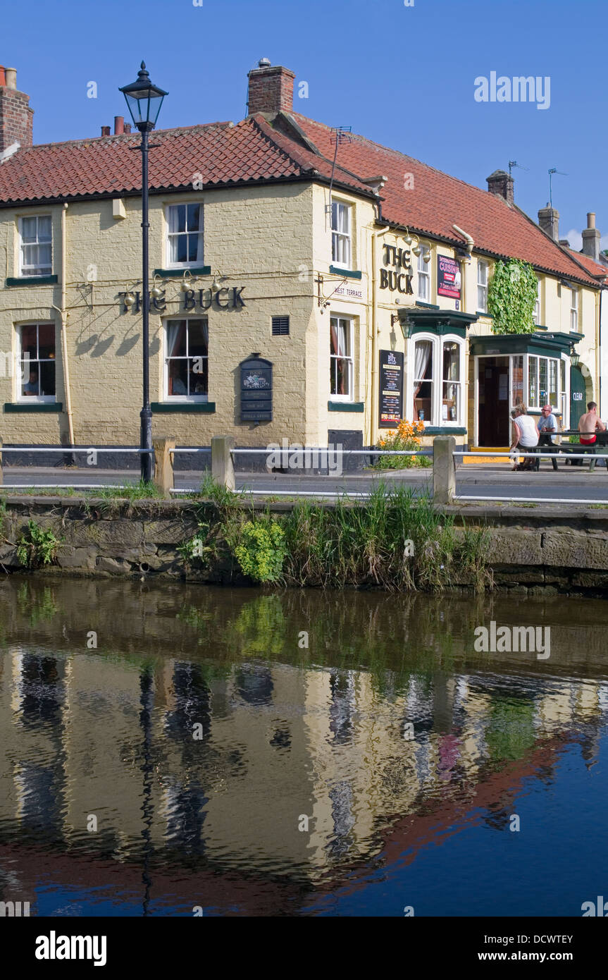 Il Buck Inn Great Ayton riflessa nel fiume Leven, caldi pomeriggi d'estate, le persone al di fuori seduta, North Yorkshire England Regno Unito Foto Stock