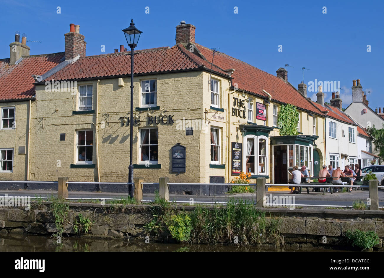 Il Buck Inn, grande Ayton, dal fiume Leven, caldi pomeriggi d'estate, le persone al di fuori seduta, North Yorkshire England Regno Unito Foto Stock