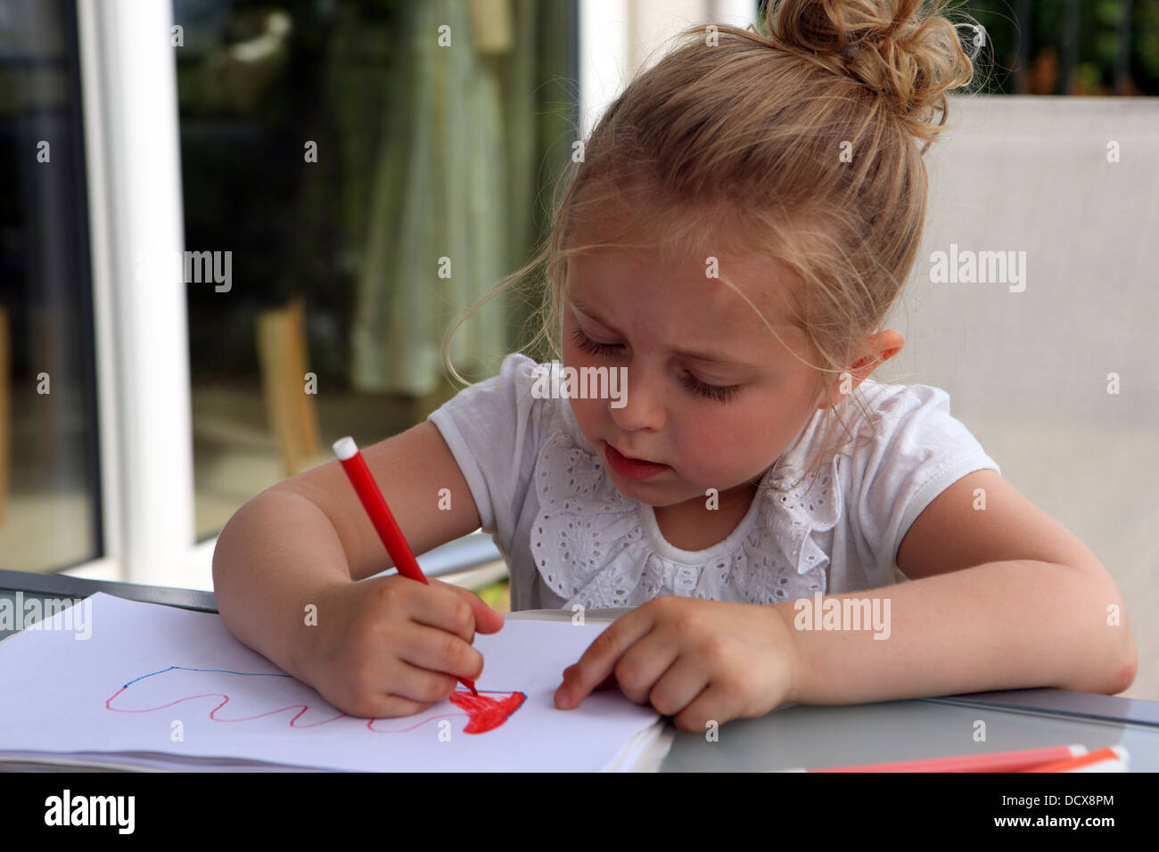 4 anno di età ragazza bionda disegno usando pennarelli su un tavolo fuori sul ponte Foto Stock