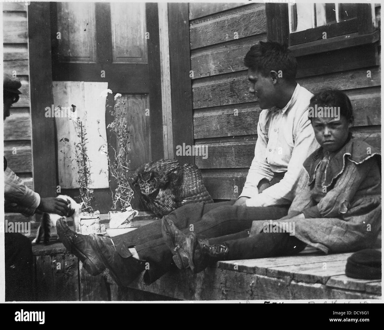 Un uomo e dei bambini indiani sono raffigurati con un gufo e un gattino, mostrando un momento culturale che coinvolge sia gli animali che i familiari. Questa immagine riflette un'interazione intima con la natura e la vita domestica. Foto Stock