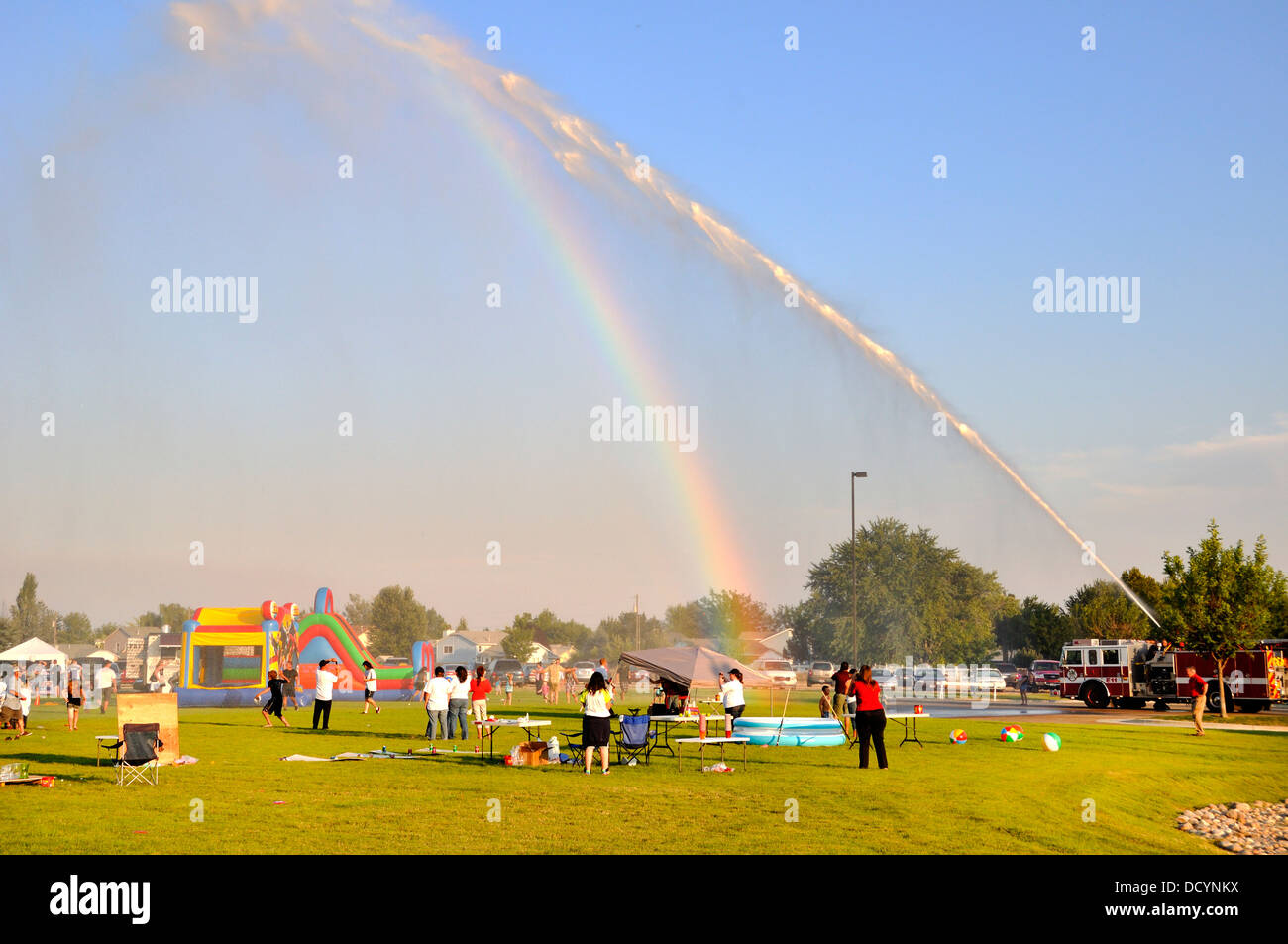 Camion dei pompieri la spruzzatura di fronte alla folla raccolta di quartiere in un caldo pomeriggio estivo Foto Stock